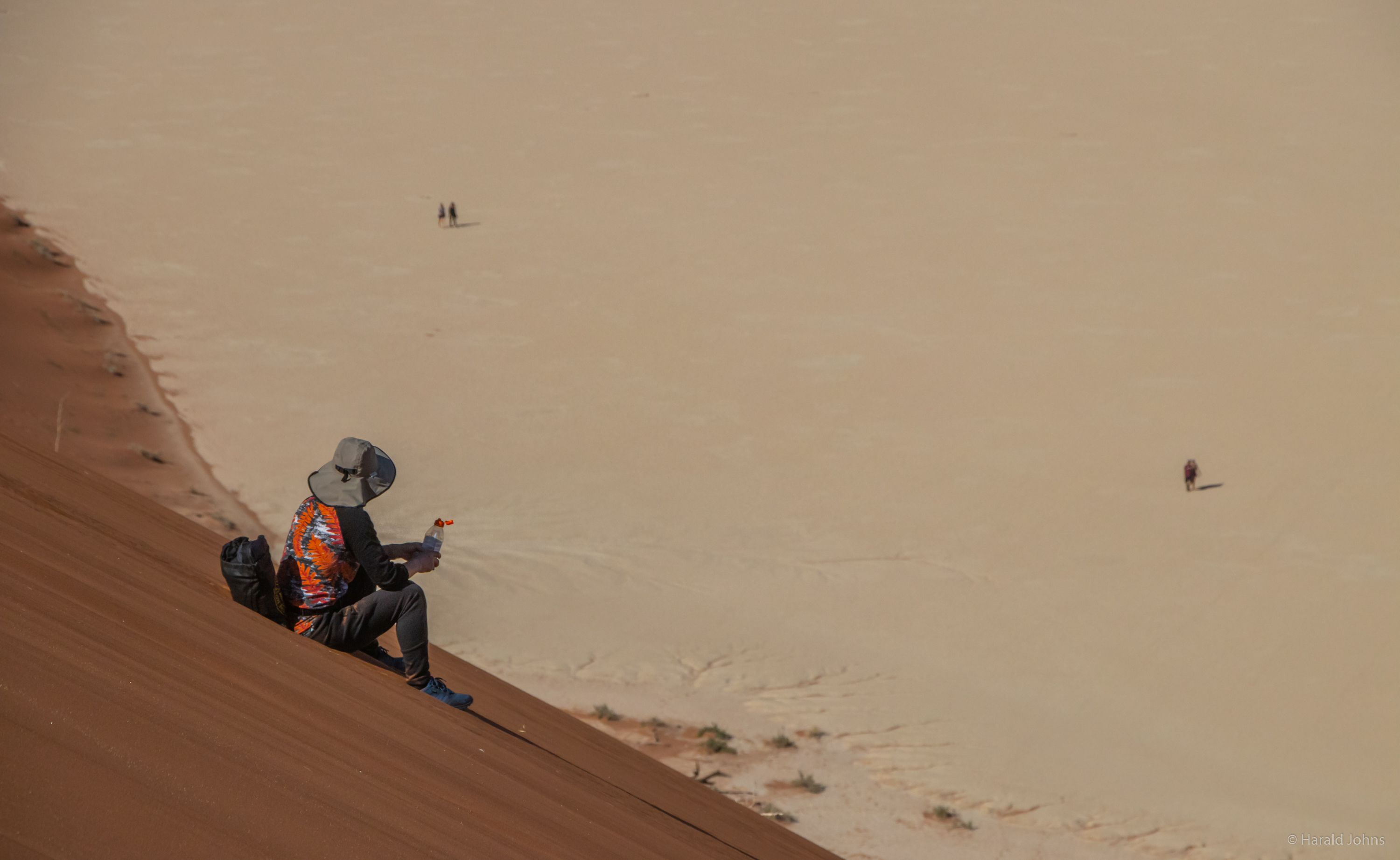Blick hinunter in das Dead Vlei, in die von hohen Sanddünen umschlossene beige Salz-Ton-Pfanne des ausgetrockneten Sees.